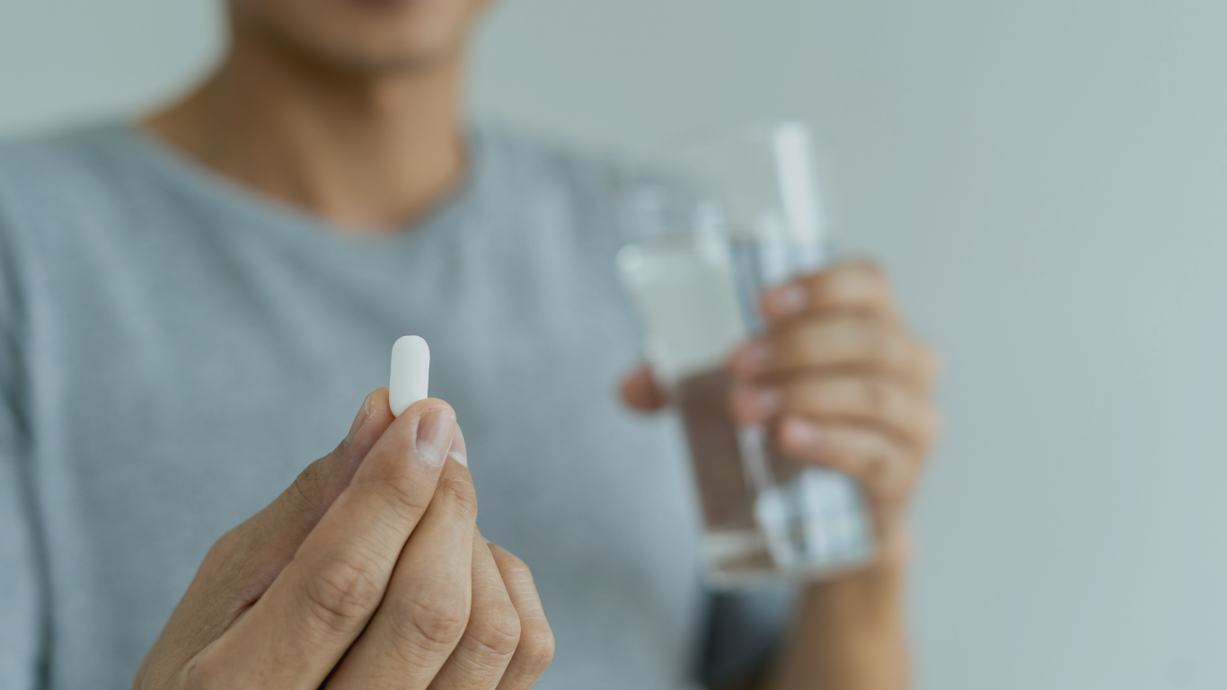 uma pessoa com um coo de água em uma mão e na outra um comprimido, pois ele está no pós-cirúrgico da cirurgia de diástase