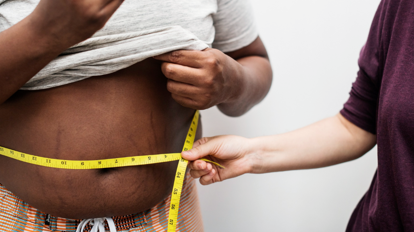 Profissional medindo a circunferência abdominal do paciente, falando sobre quando o sobrepeso é considerado risco à saúde