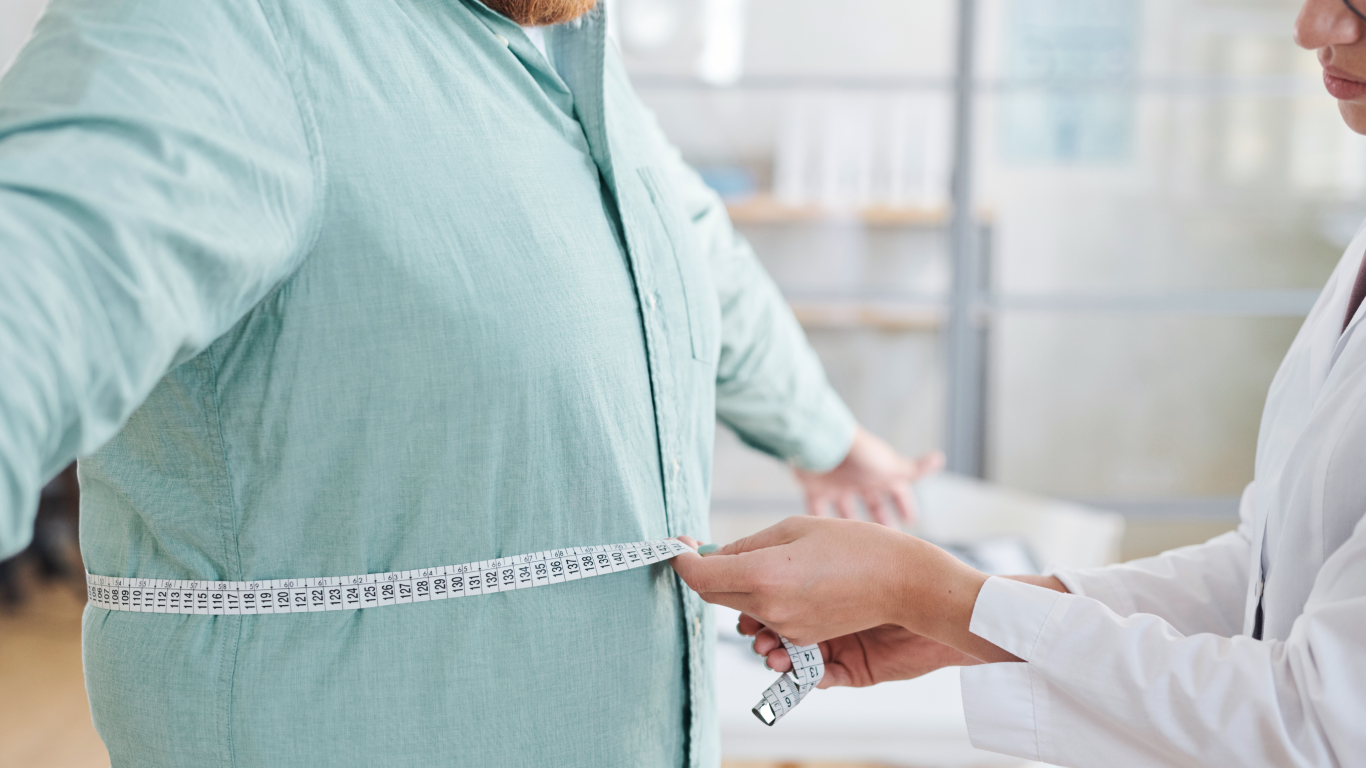 Profissional medindo a circunferência abdominal do paciente, explicando riscos e benefícios da cirurgia bariátrica
