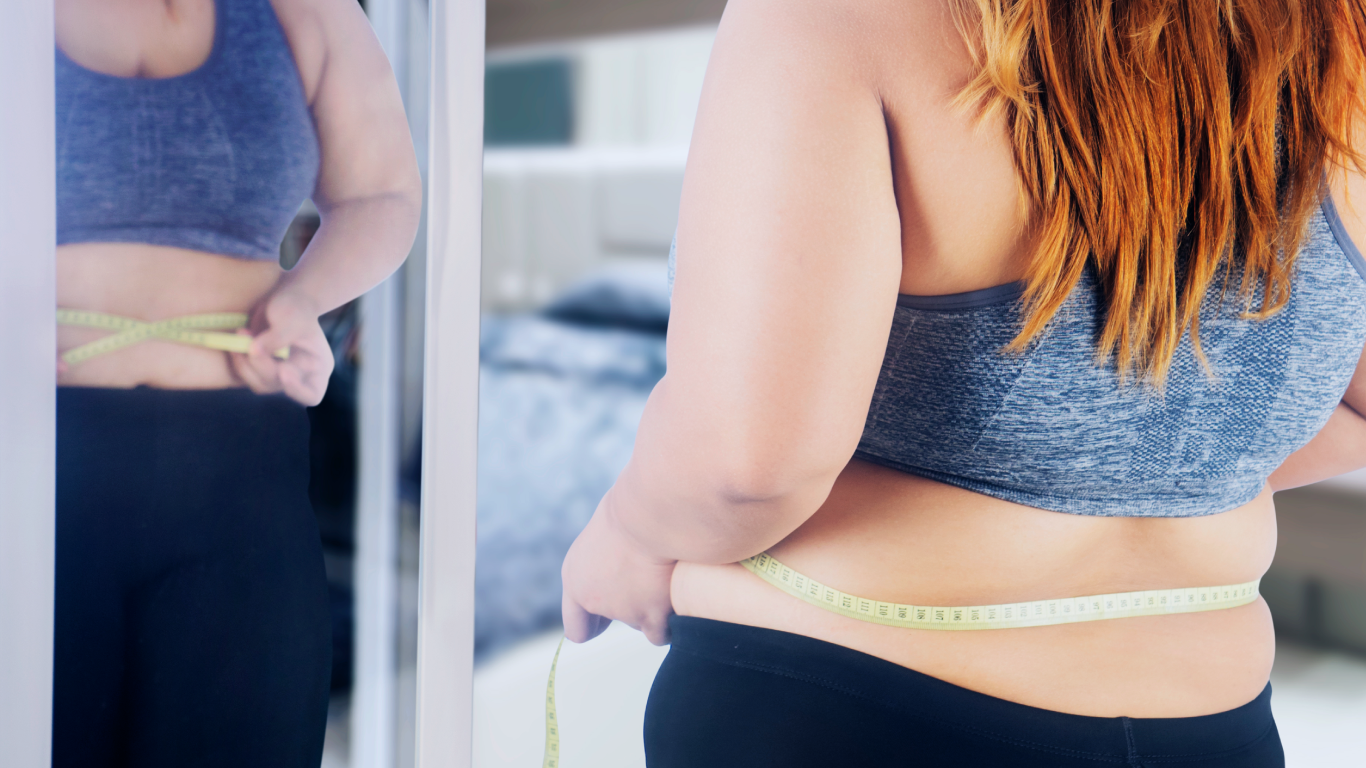 Mulher em frente o espelho, medindo a circunferência abdominal, pensando nas indicações para a cirurgia bariátrica