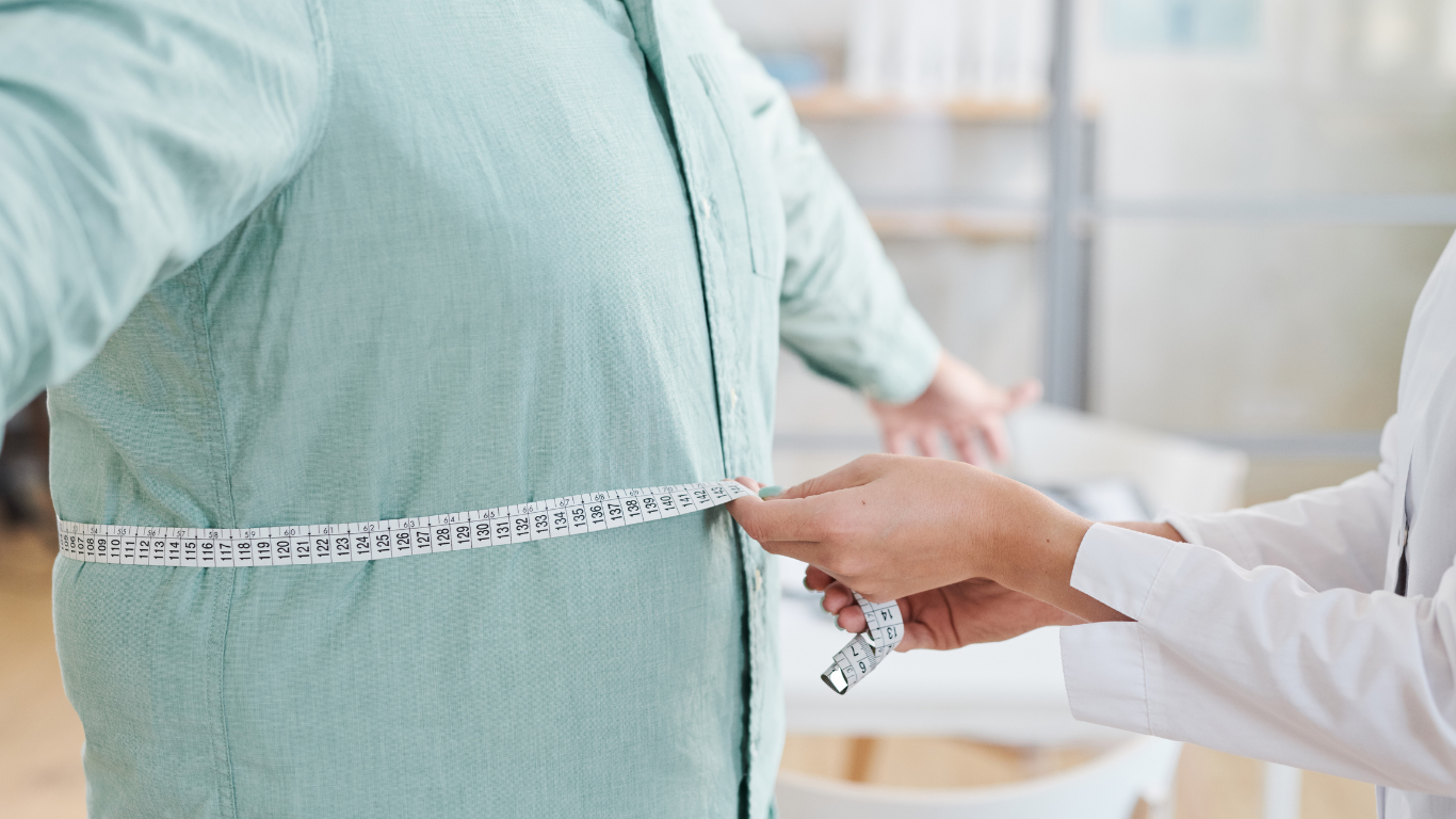 Médico medindo a circunferência abdominal do paciente, explicando os riscos da cirurgia bariátrica